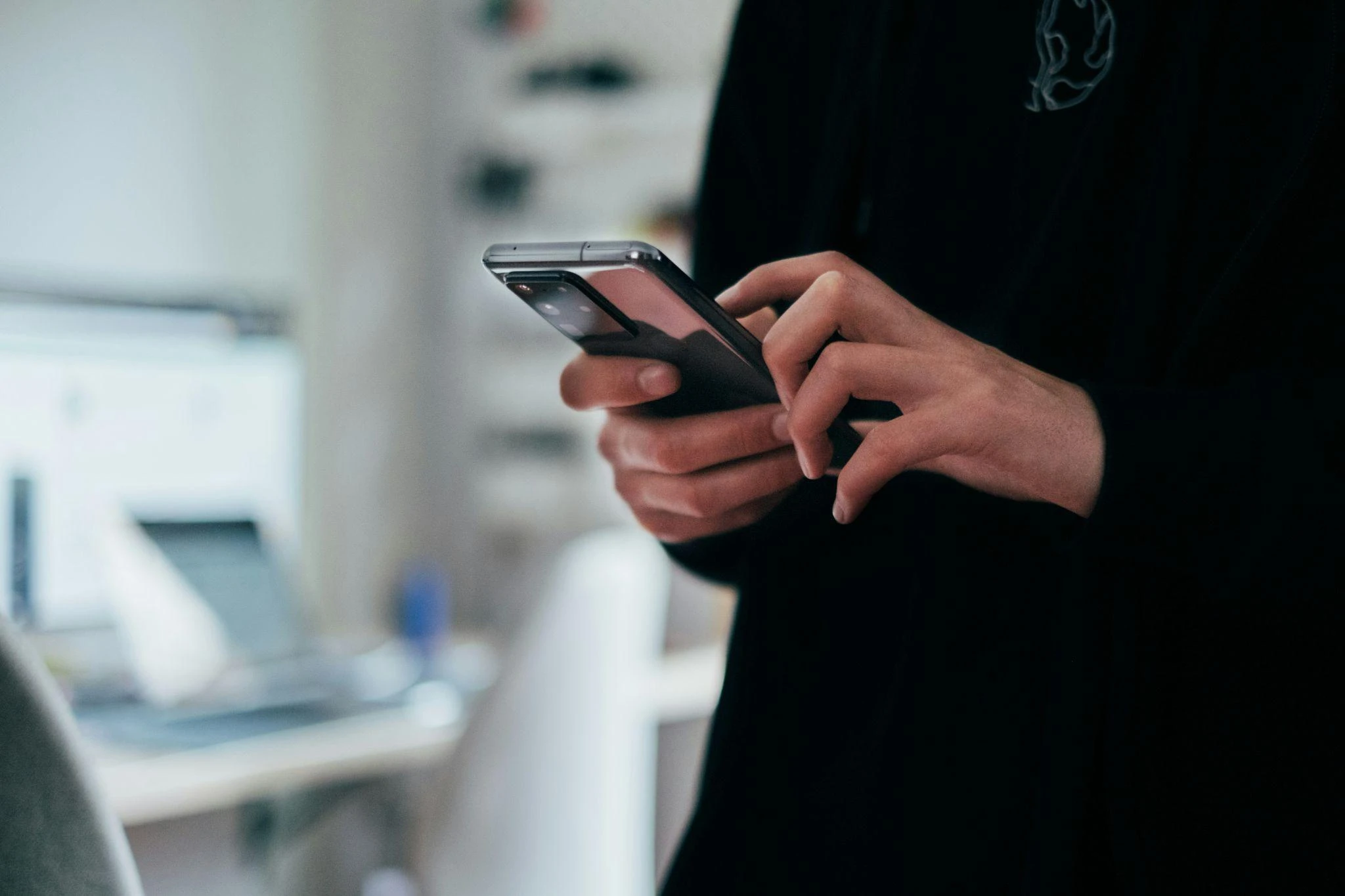 Kvinne bruker mobiltelefon ved et skrivebord
